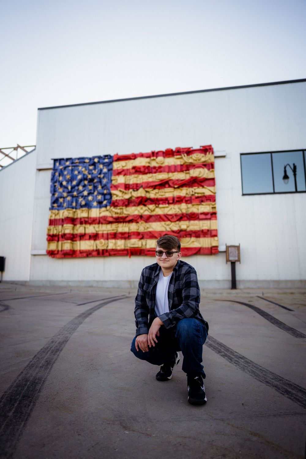 Person poses in front of large American flag artwork on white building exterior.