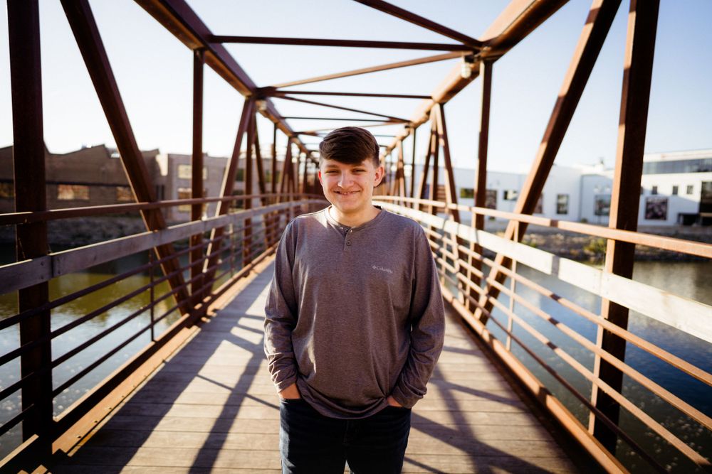 Person stands on rustic metal bridge with industrial architecture in background.