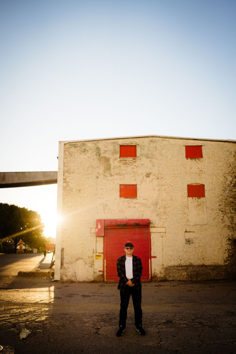 Dramatic sunset portrait in front of industrial building with red doors and windows.