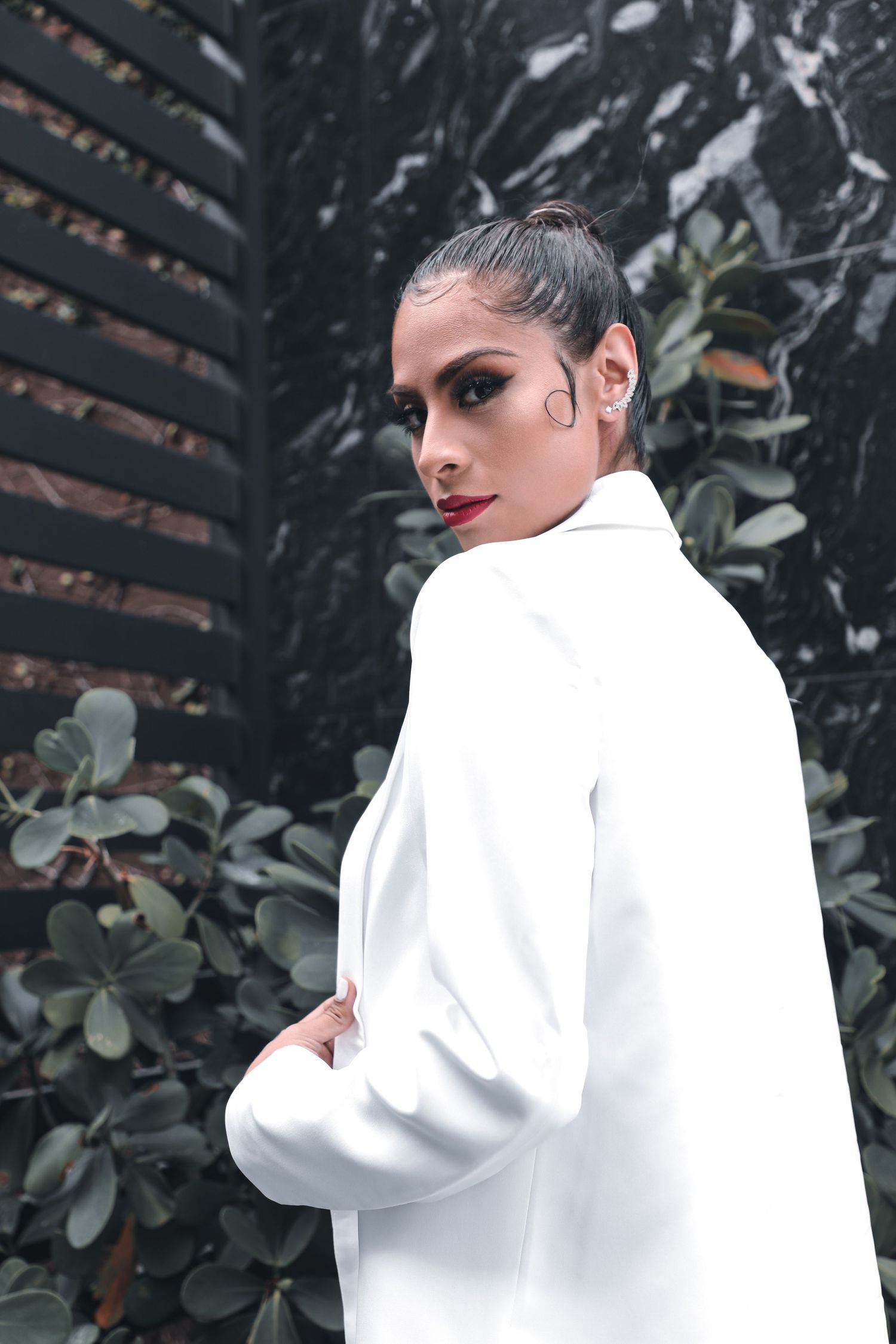 Fashion portrait of model in white coat against dark marble and wood panel wall.
