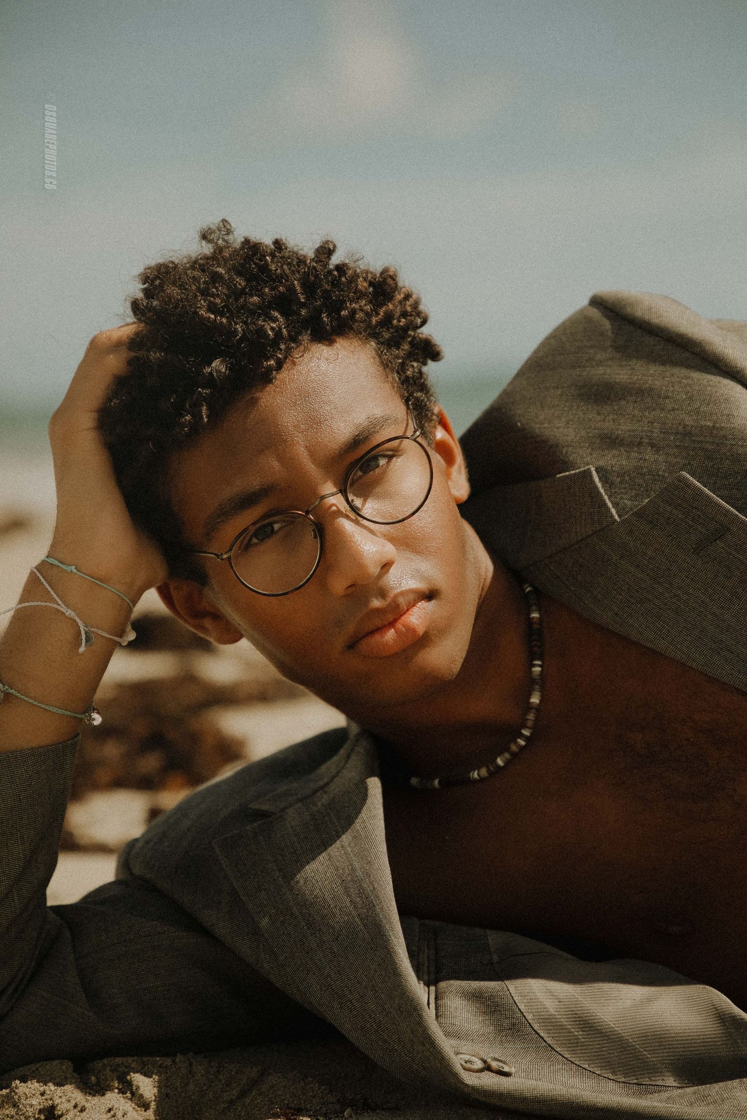 Artistic portrait of person in glasses and denim jacket laying on sand during golden hour.