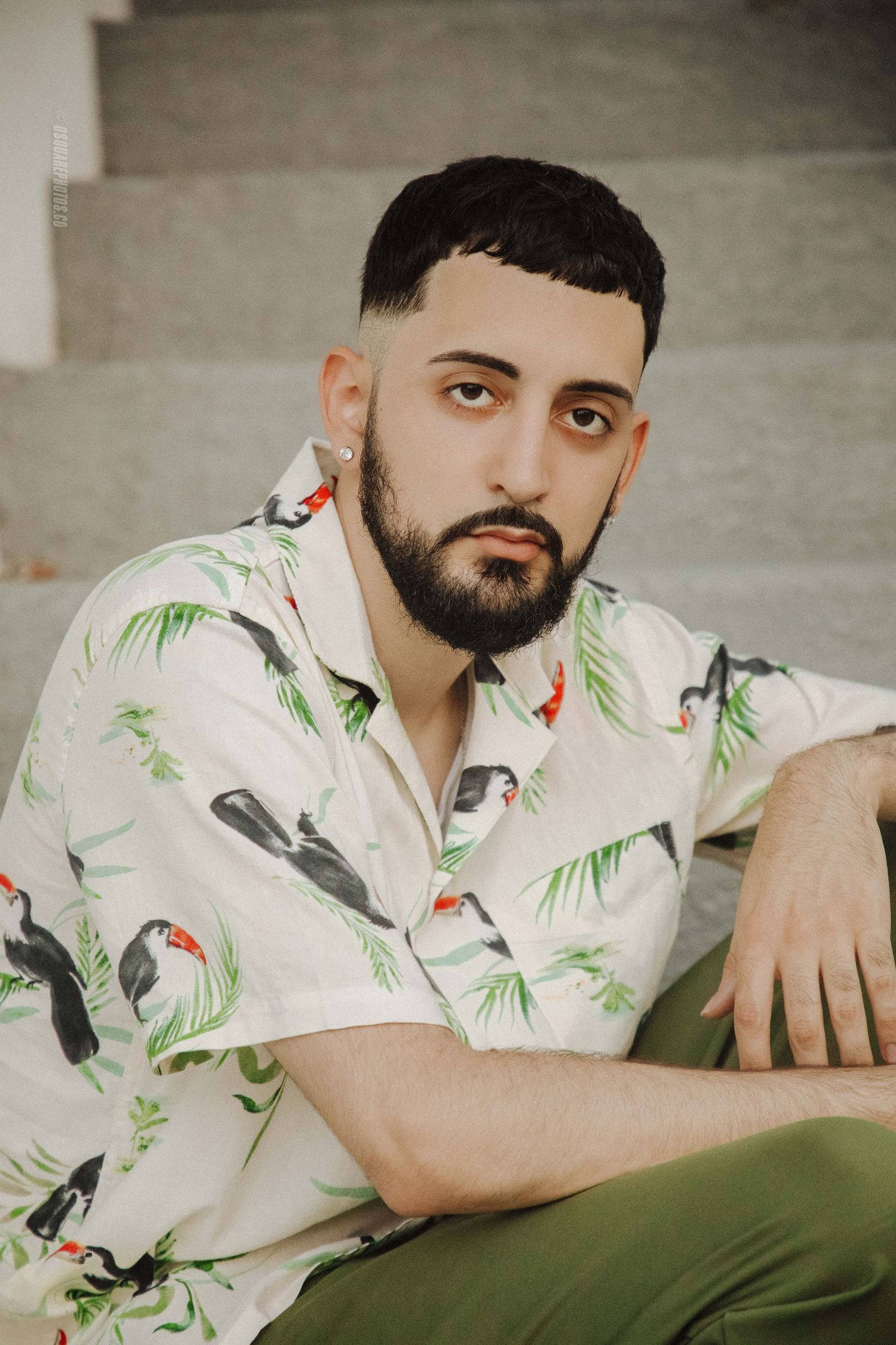 Portrait of person in tropical print shirt with palm trees and birds against grey background.