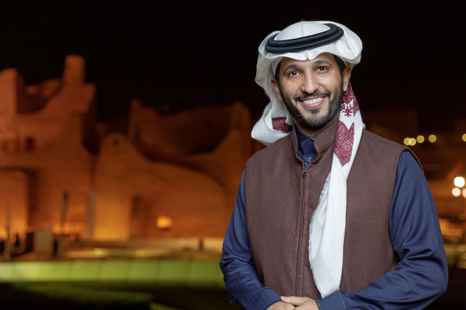 Person in traditional Middle Eastern dress at night with buildings in background.