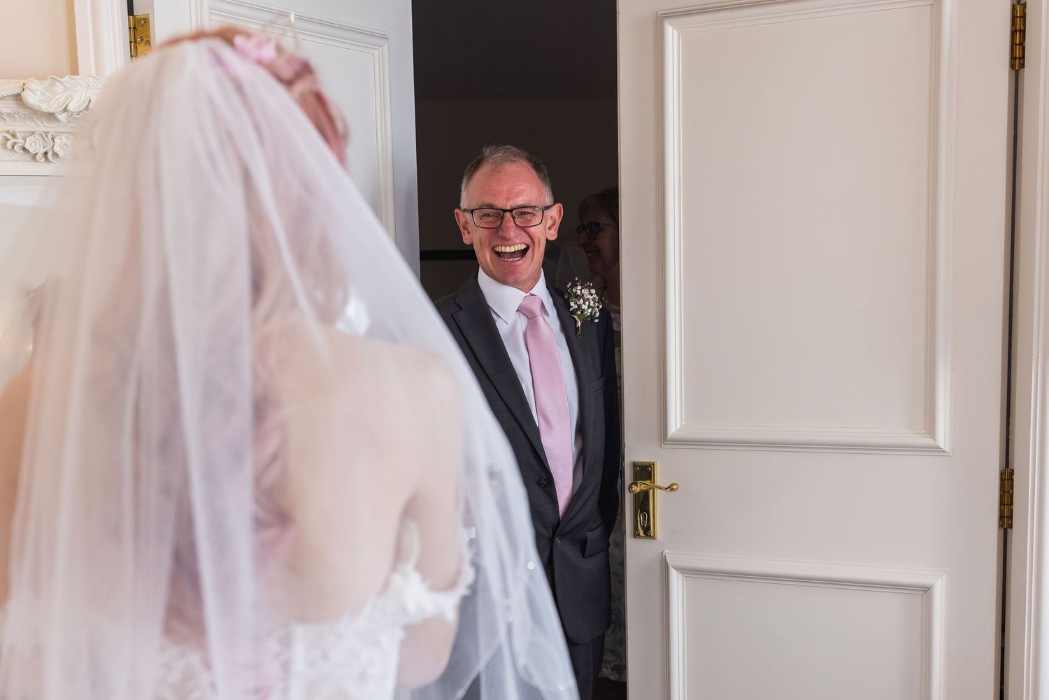 Father smiling happily looking at his daughter in her wedding dress for the first time with a pink tie