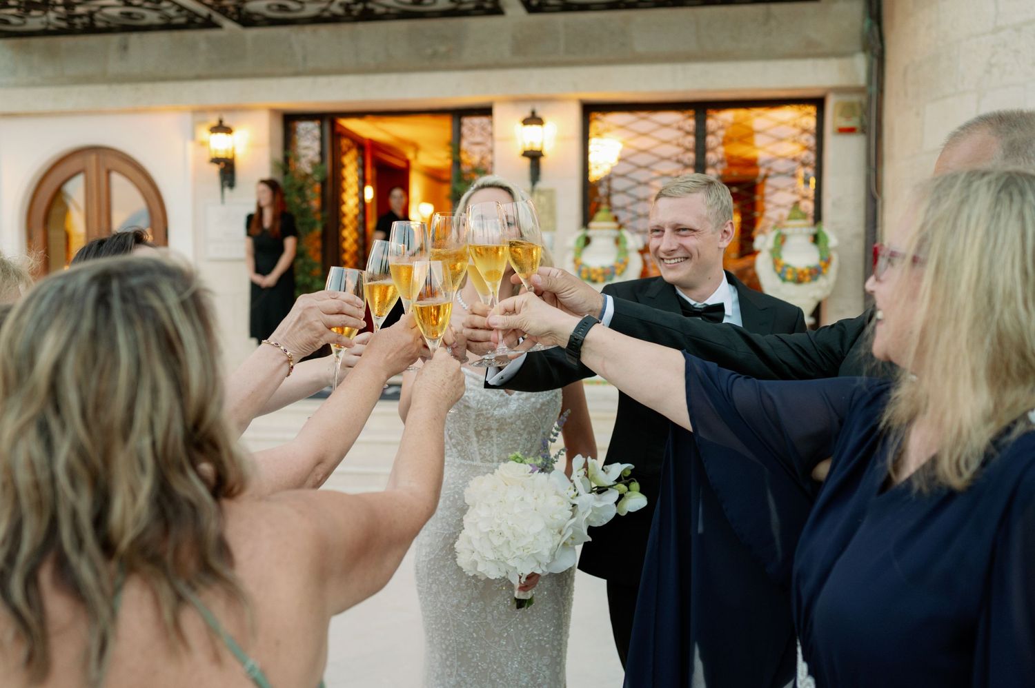 Wedding guests raising champagne glasses in celebratory toast outdoors.