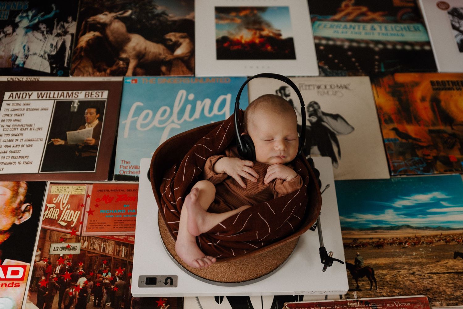 newborn baby with headphones on nestled in a bowl on a turntable