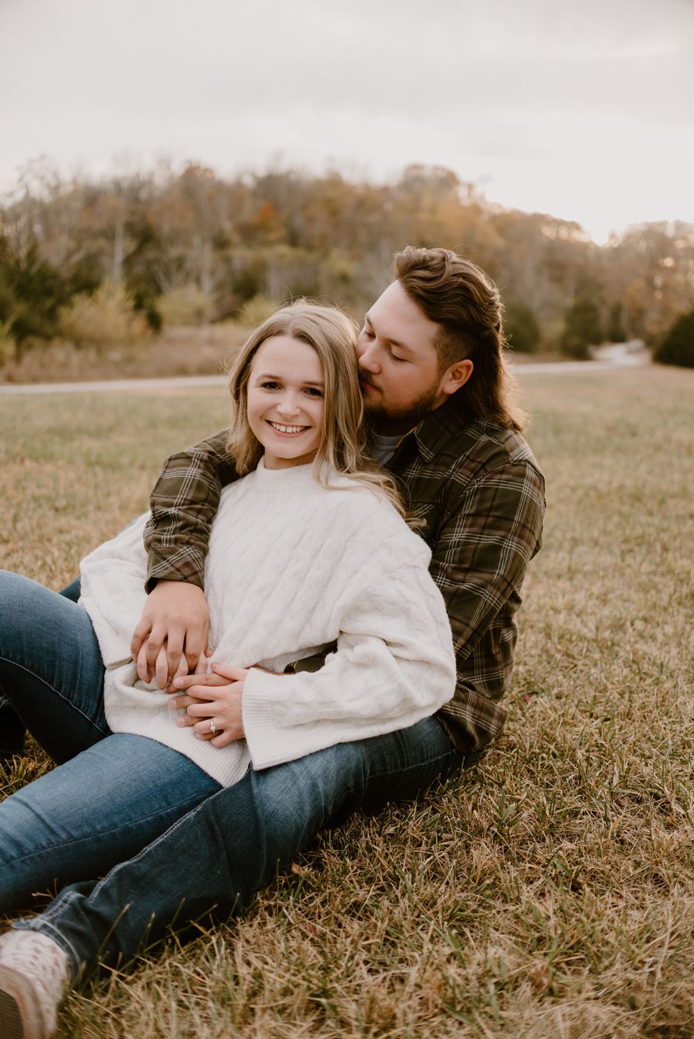 Couple relaxes together in a sunny field wearing casual autumn clothing.