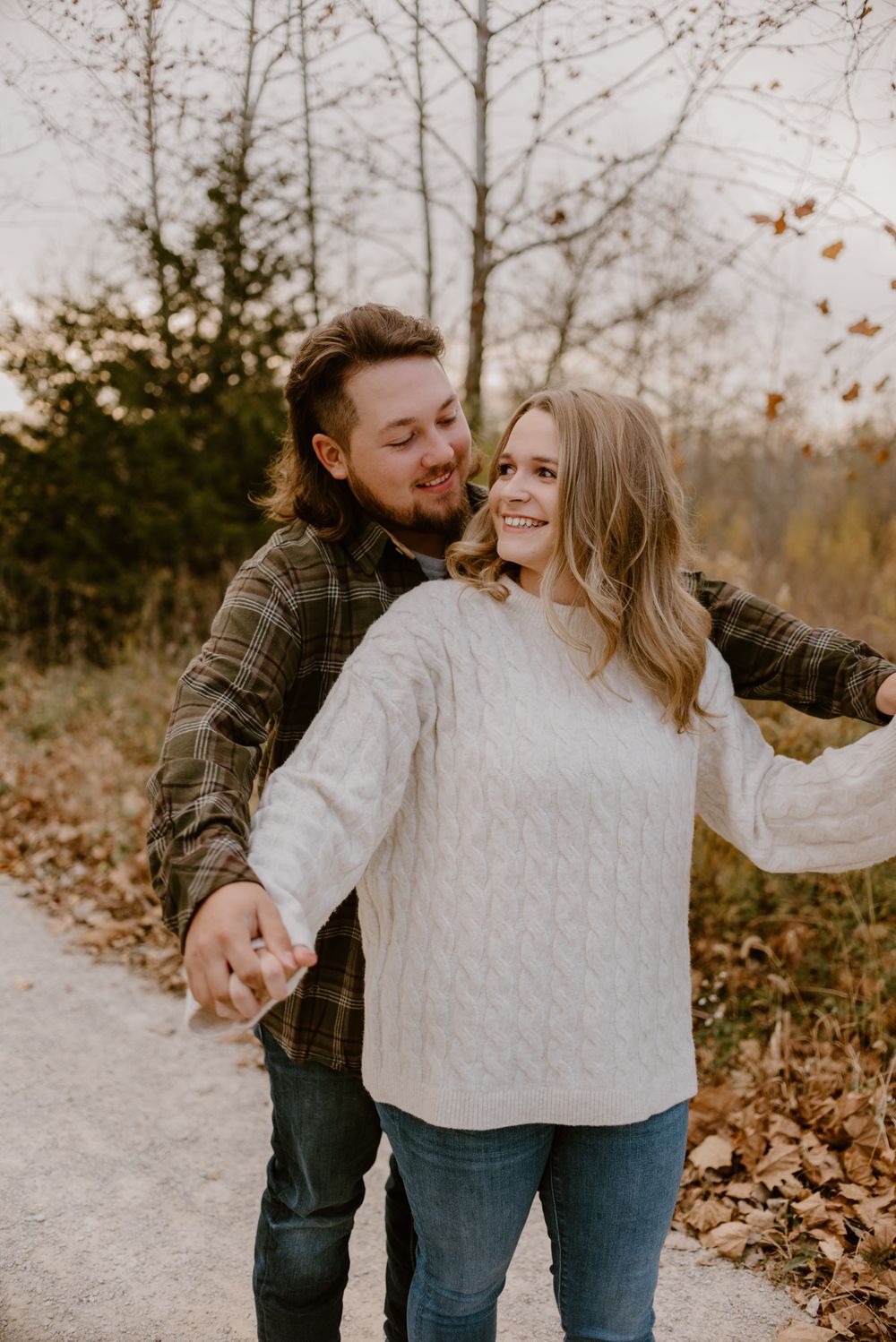 Playful couple shares joyful moments on a path surrounded by fall foliage.