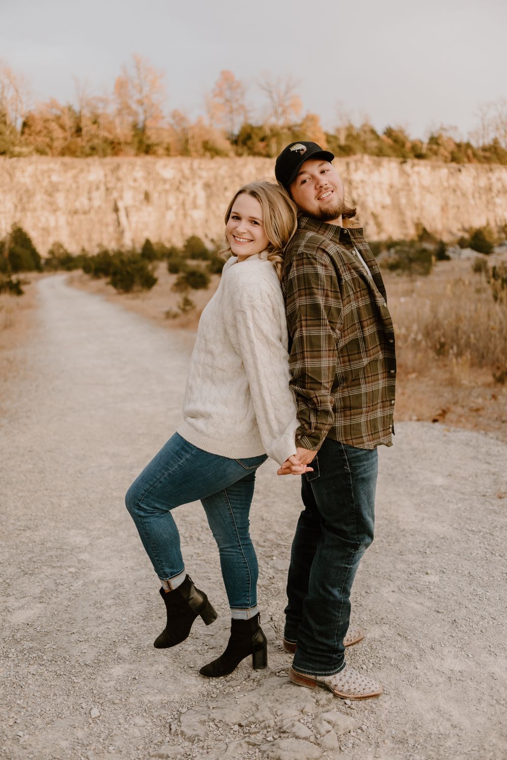 Couple playfully walks along a dirt path in casual denim and sweater outfits.