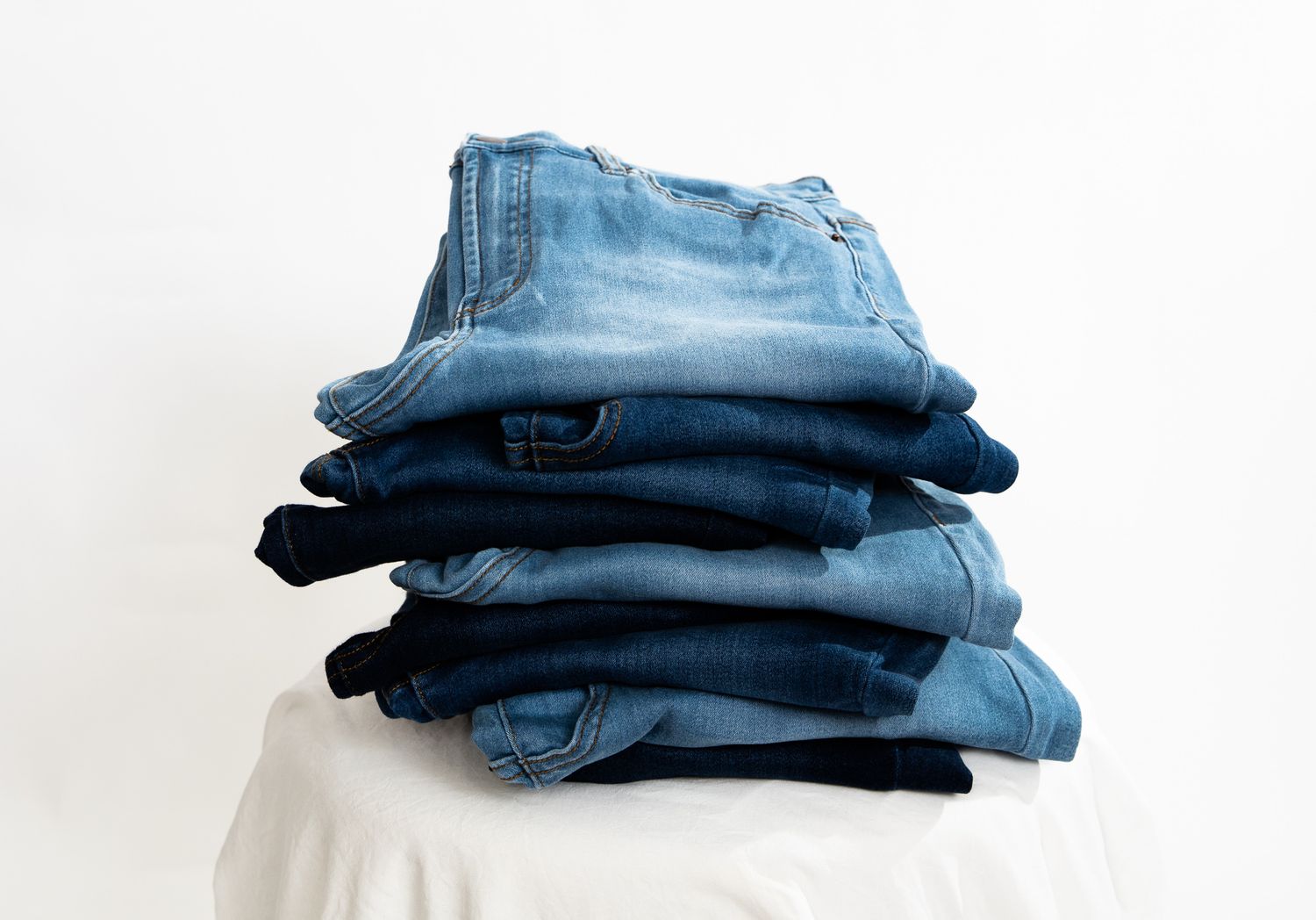 Product shot of 8 pair of blue jeans staked together