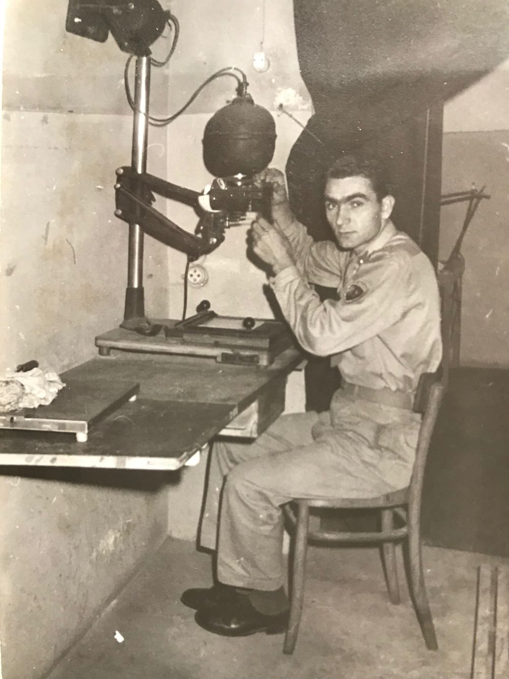 People working at vintage photo enlarger stations in a darkroom laboratory setting.