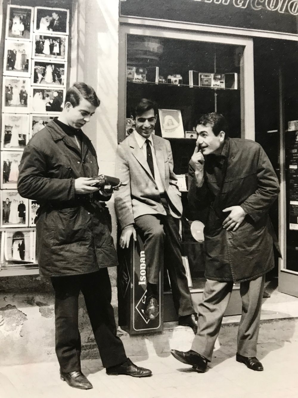 Group of people gathered outside a photo studio examining prints in the 1950s.