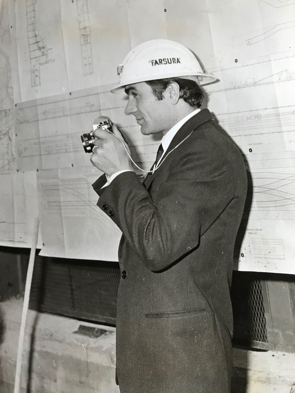 People examining architectural drawings or blueprints on wall in vintage photograph.