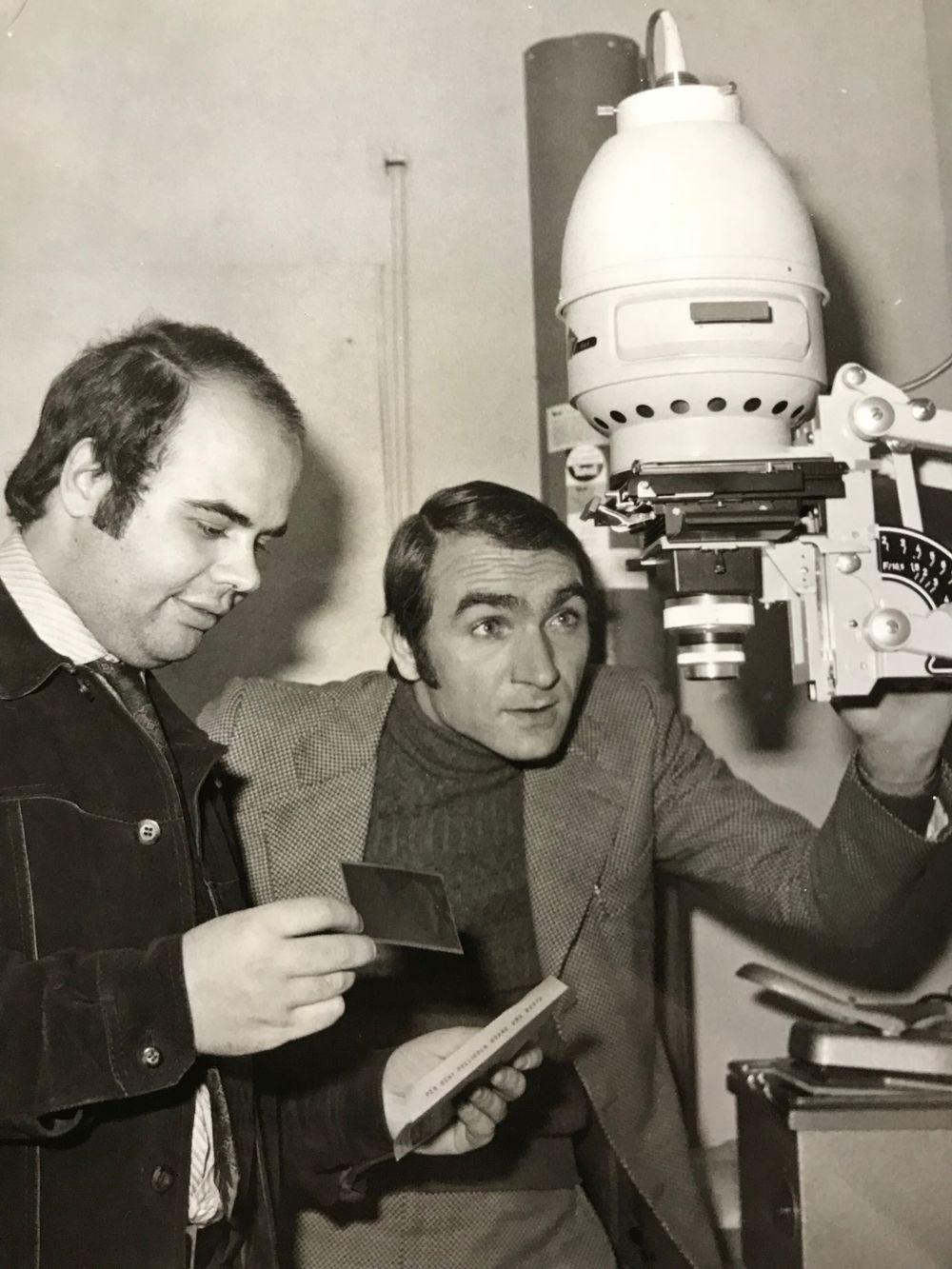 Two people examining photographic equipment in studio setting.