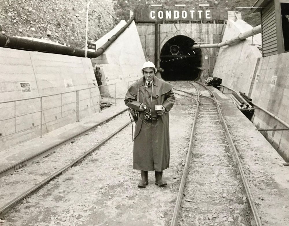Black and white photograph of person walking along narrow urban pathway.