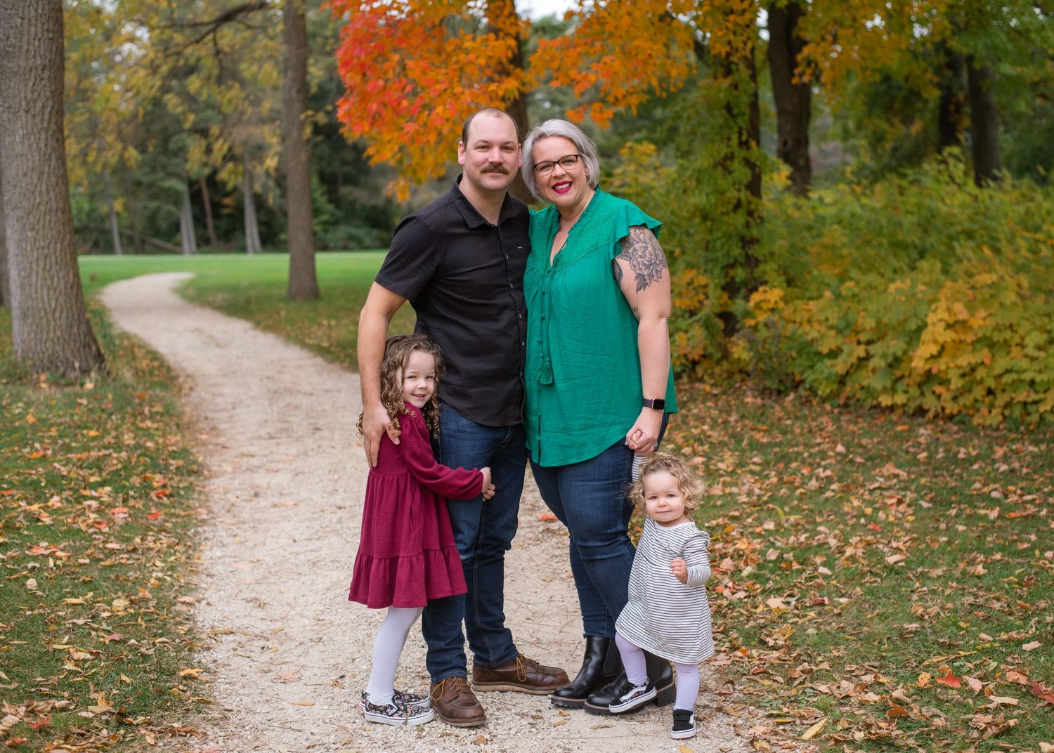 A family portrait on an autumn path with vibrant orange and yellow fall foliage in background.