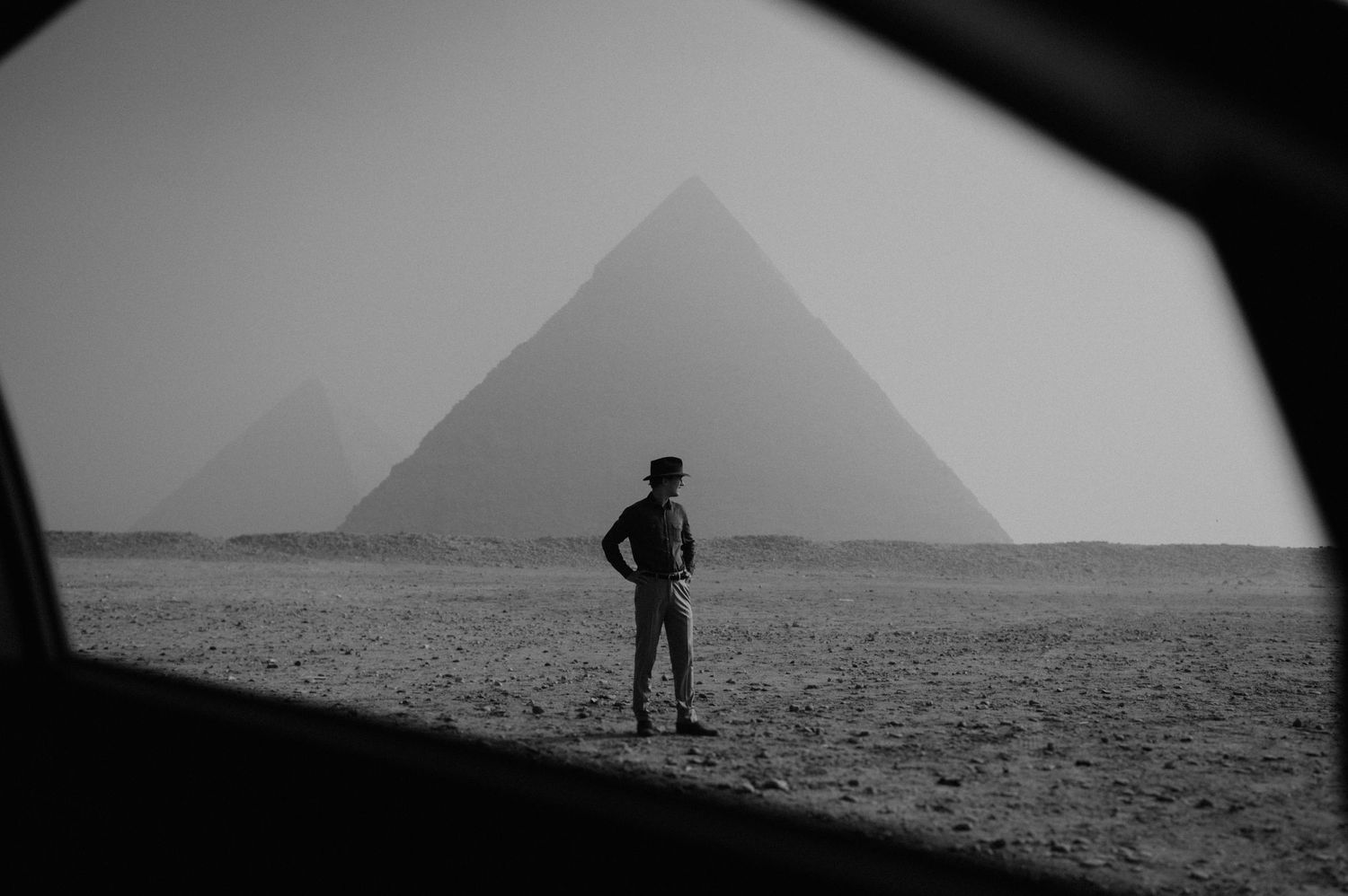 A silhouetted figure stands before the pyramids of Giza in a moody black and white photograph.