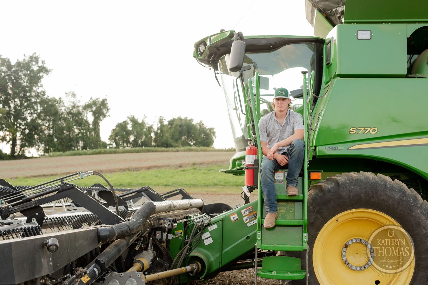Large green John Deere combine harvester parked in a rural field during harvest season.