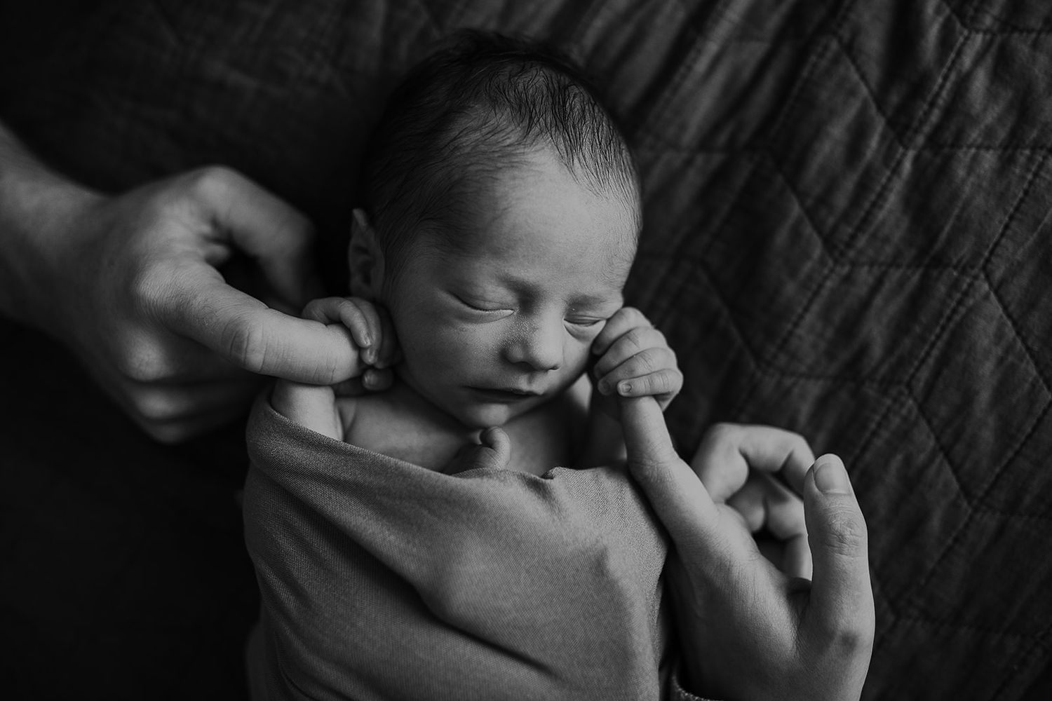 A newborn baby boy holds on tightly to his mother and father's fingers.