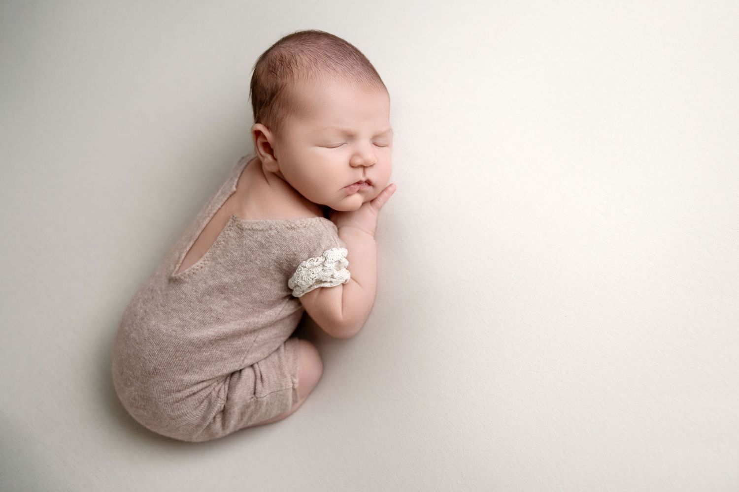 Peaceful sleeping newborn baby wrapped in soft beige fabric against white background.