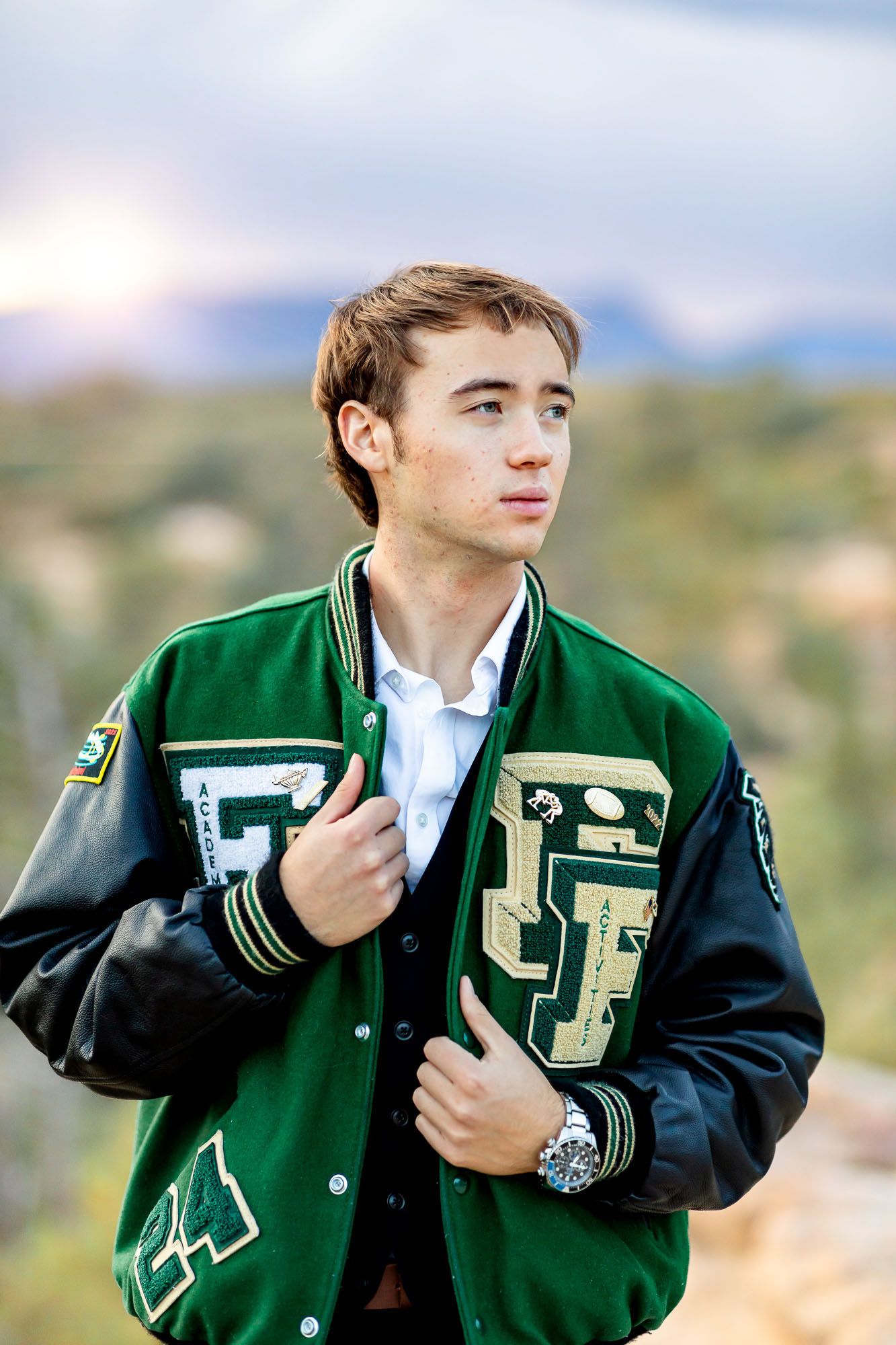 Senior guy poses in letter jacket and looks to the side at his senior session at Palmer Park in Colorado Springs.