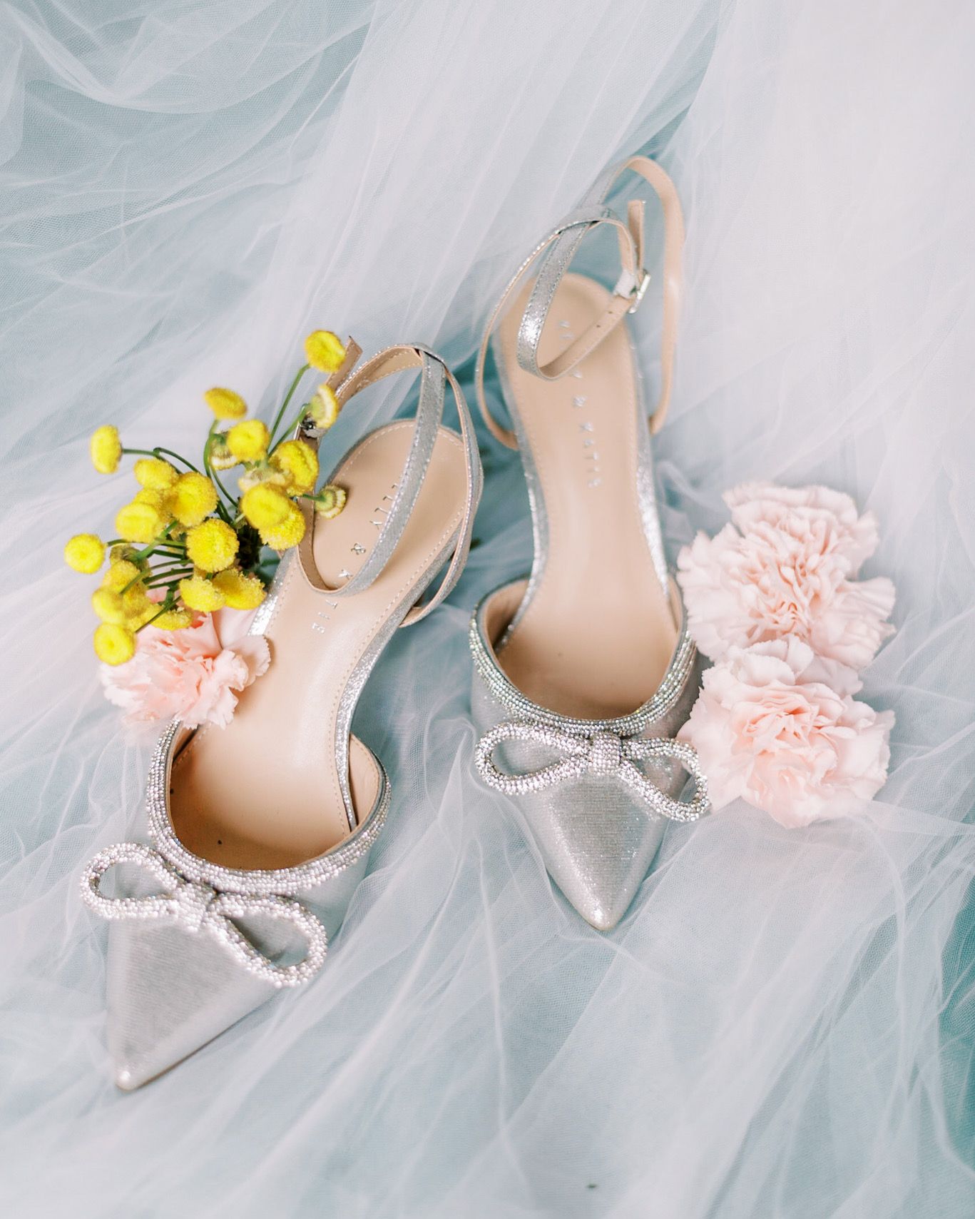 Silver bridal shoes with bow detail styled with yellow flowers and tulle.
