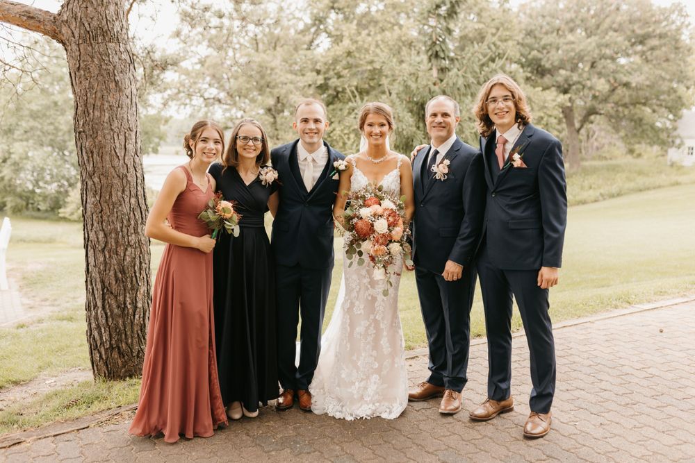 Bride and groom with four family members smiling together outdoors at a garden wedding venue.