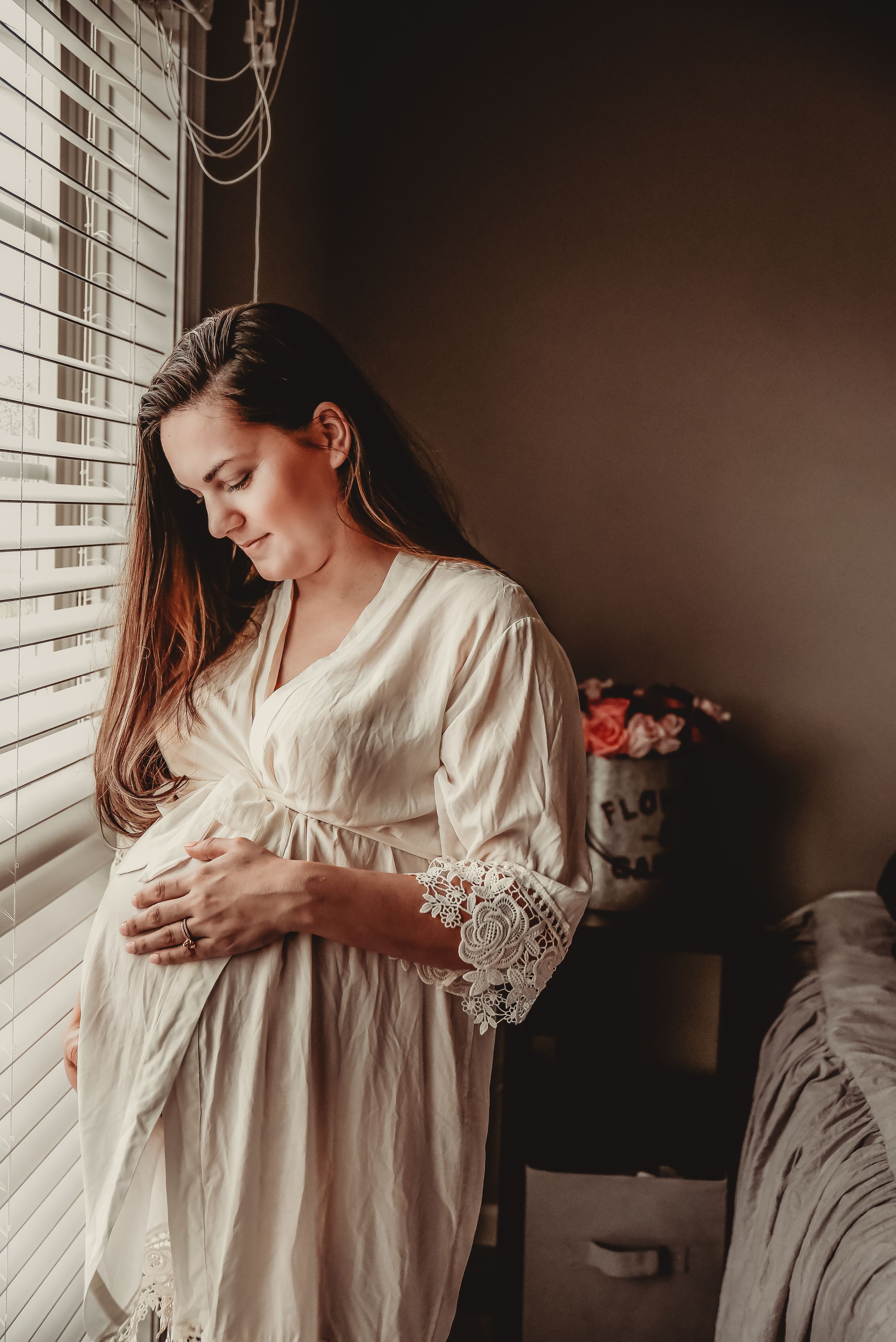 Woman in vintage white dress posing by window in moody lighting.