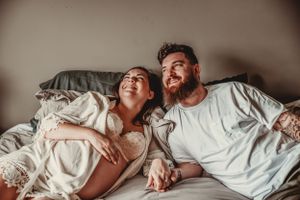 Intimate couple's maternity photos captured on bed with natural lighting.