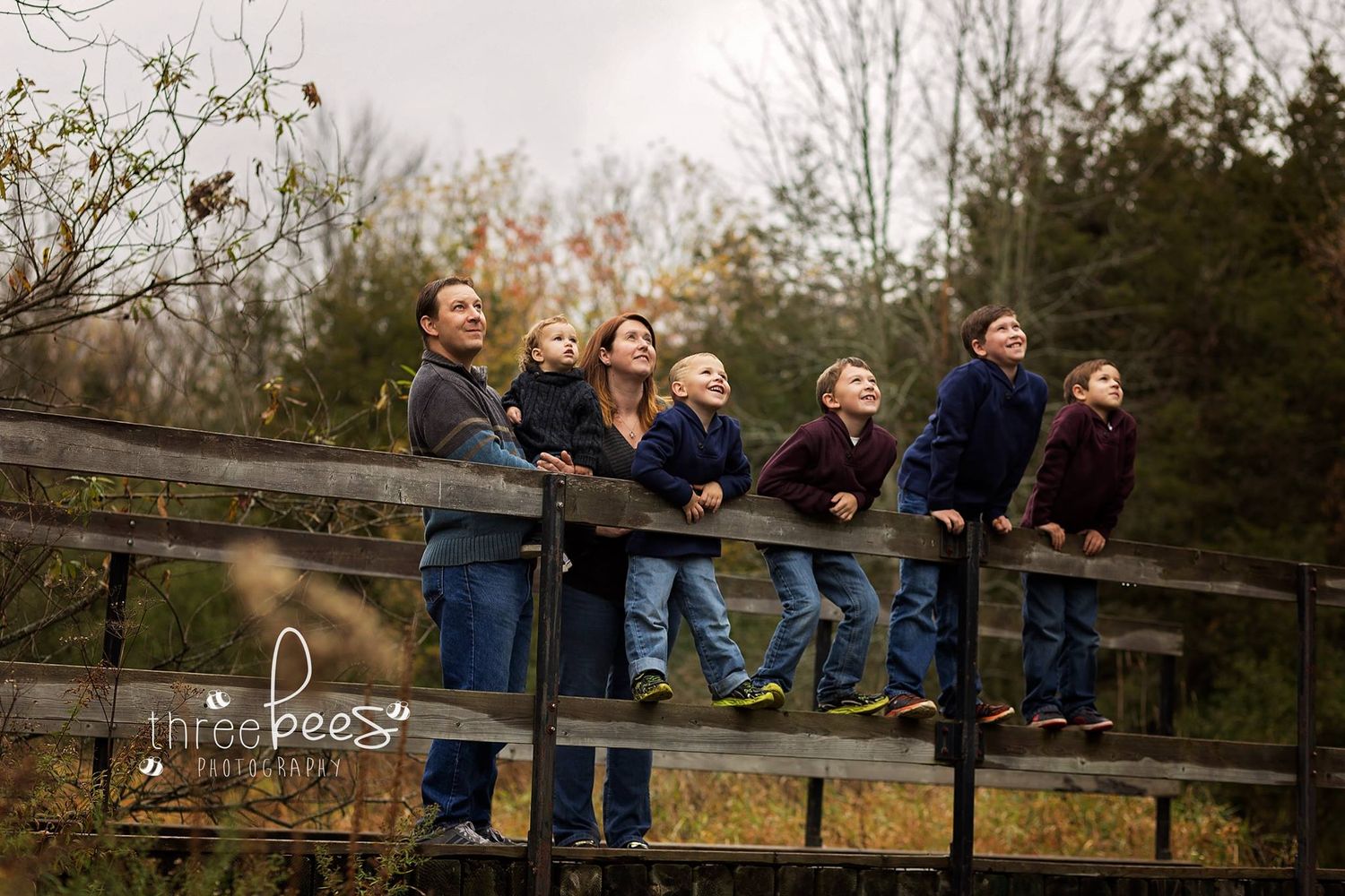 A group poses casually on a wooden fence in an outdoor autumn setting.