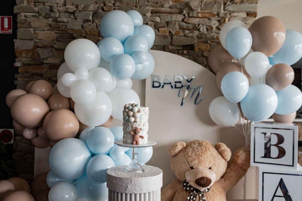 Baby shower decorations featuring blue and white balloon arches with teddy bear accents.