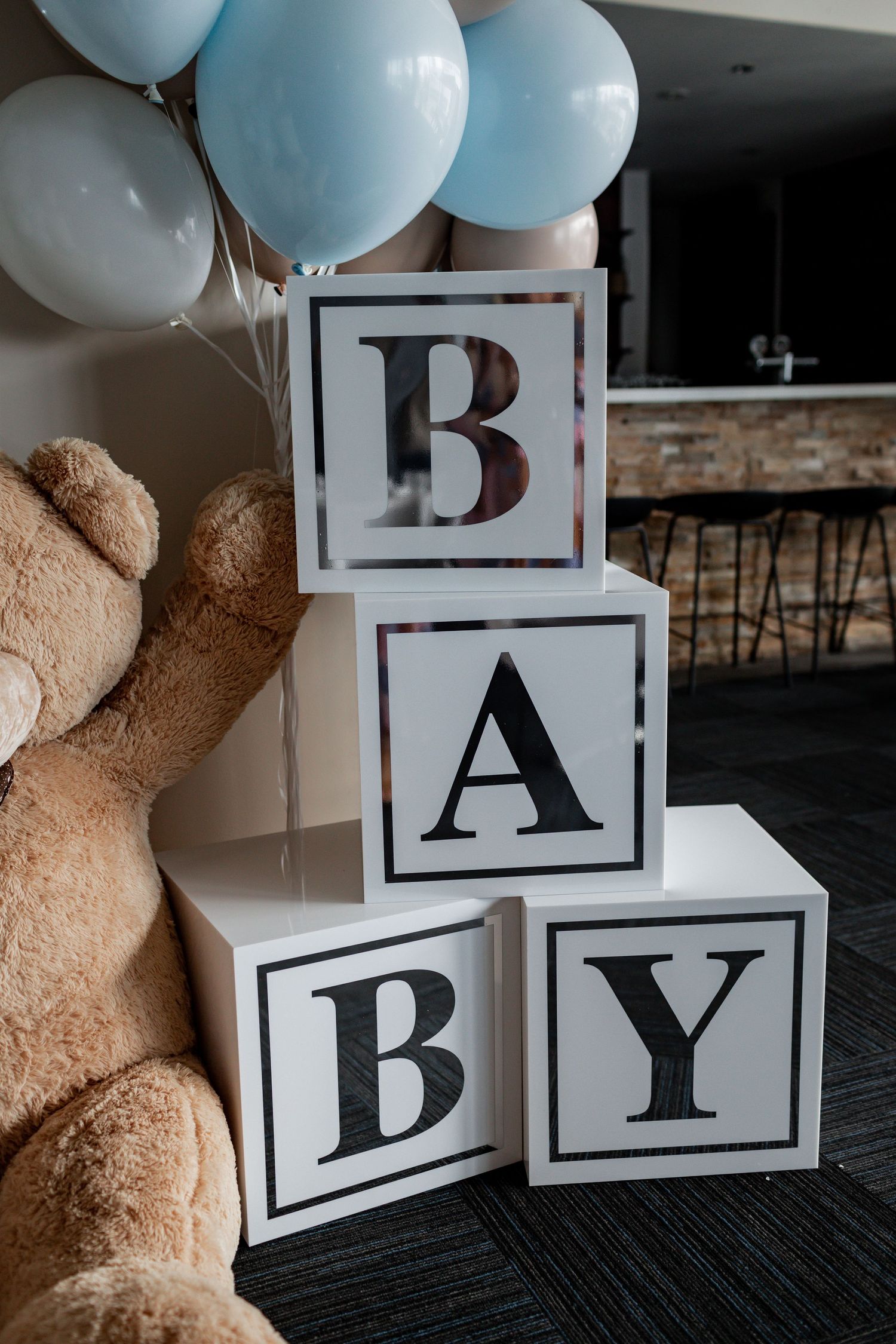 White decorative blocks spelling 'BABY' with blue balloons and teddy bear beside them.