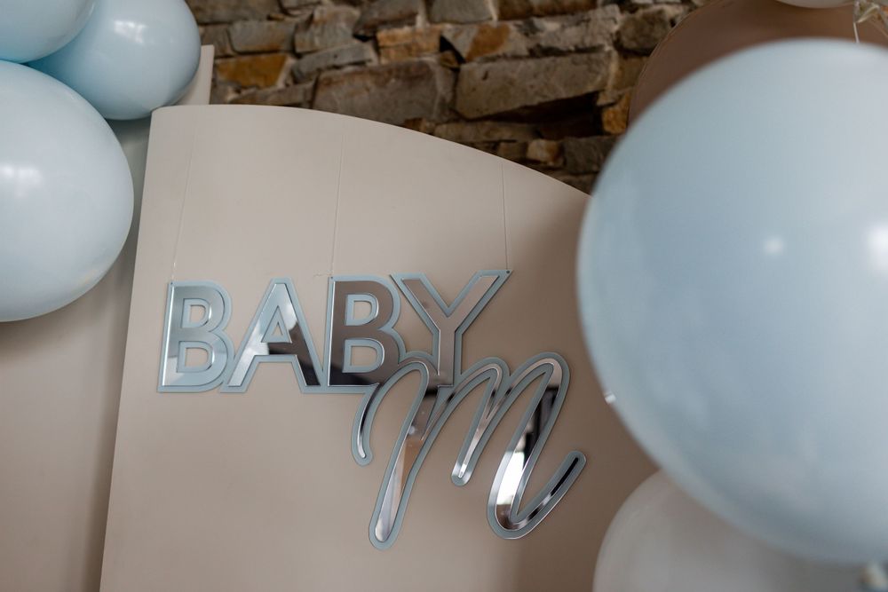 Silver 'BABY' text decoration with light blue balloons against a rustic stone wall background.