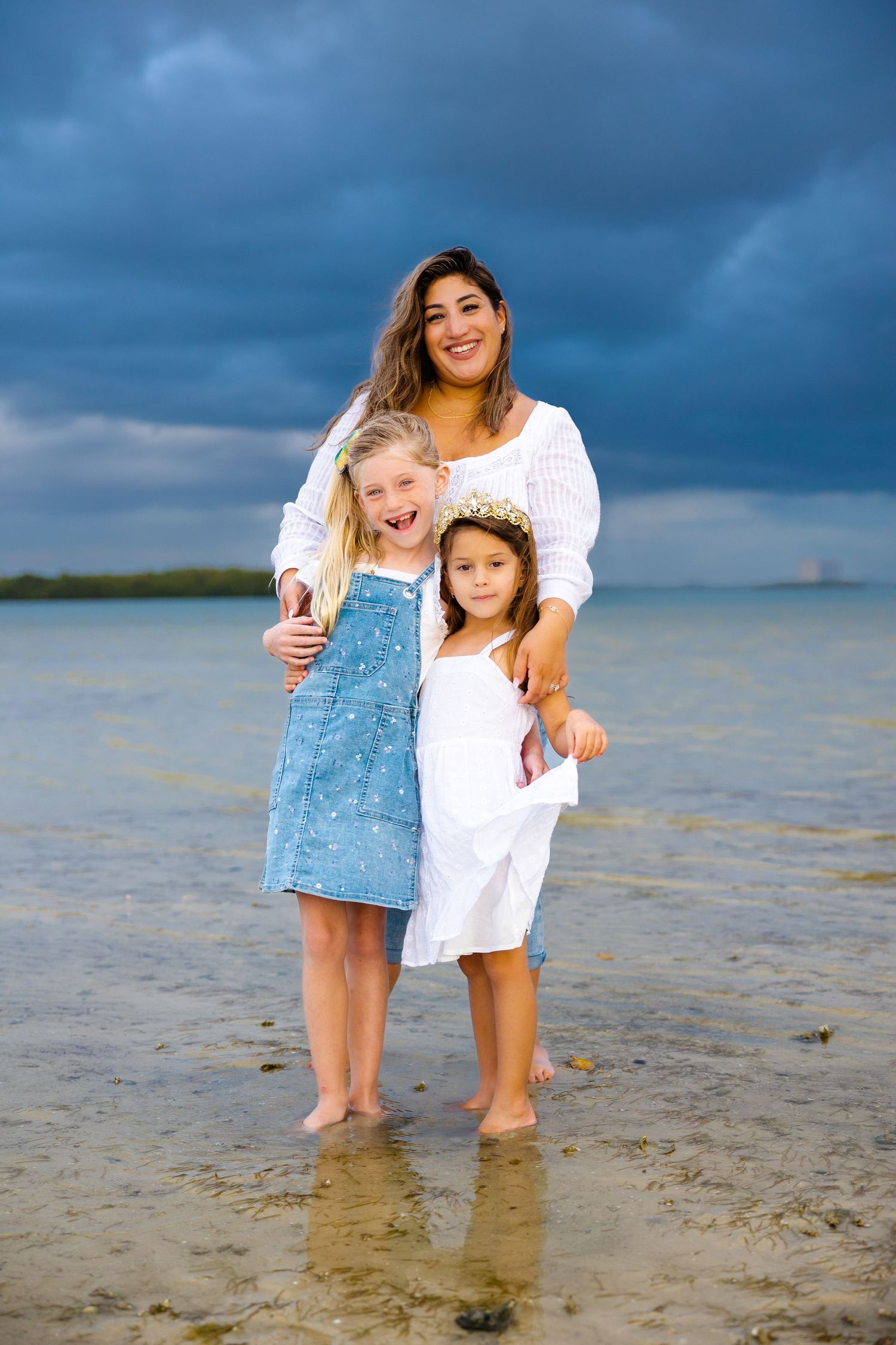 mom with her daughters smiling on the beach