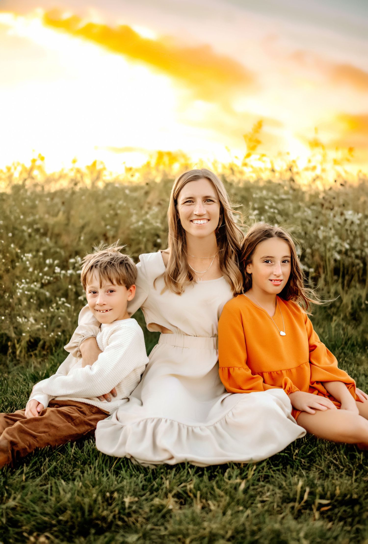A family portrait in a wildflower field at sunset wearing coordinated neutral and orange outfits.
