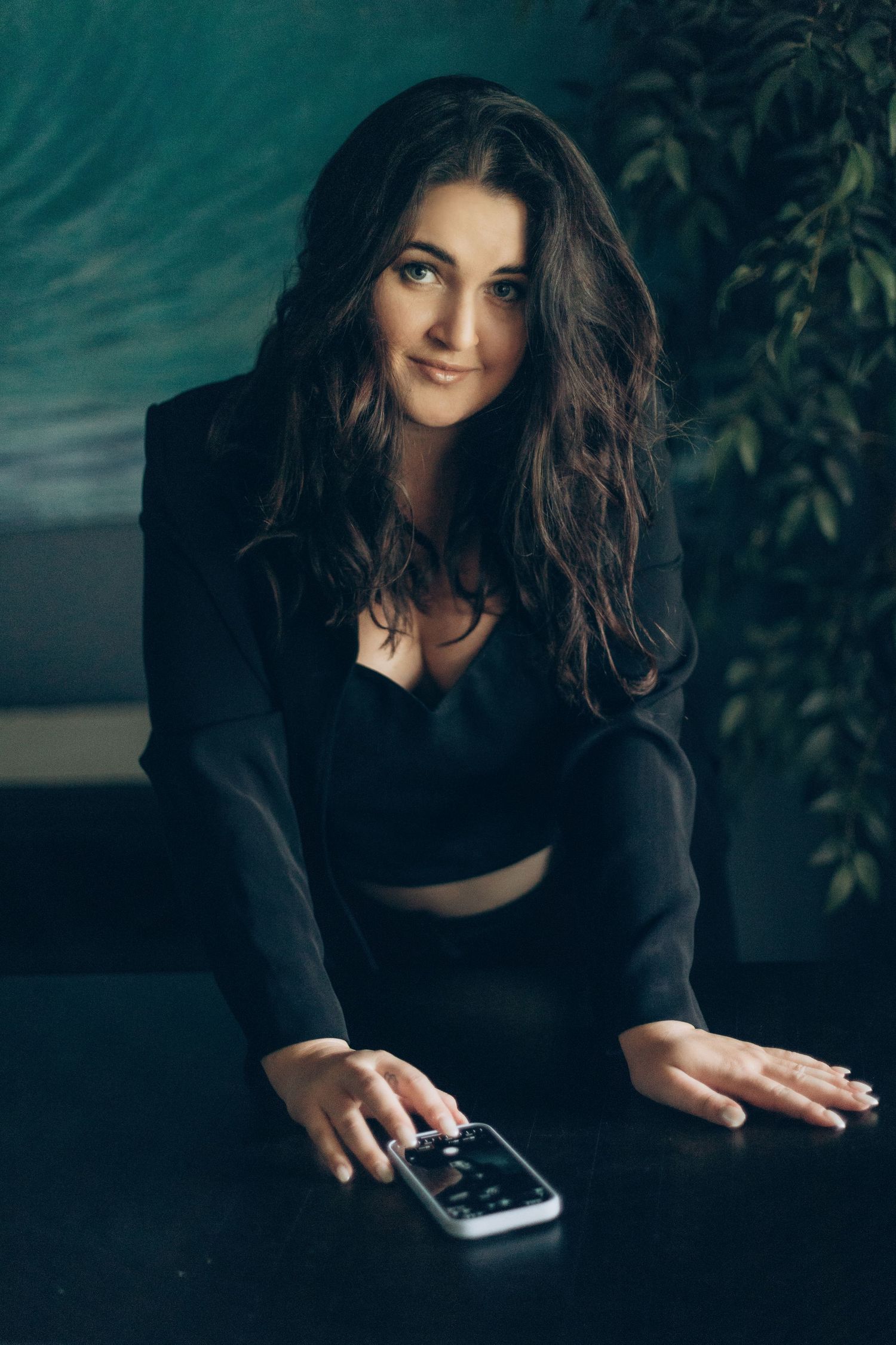 A fashion portrait in dark setting with figure in black outfit reaching for remote control.