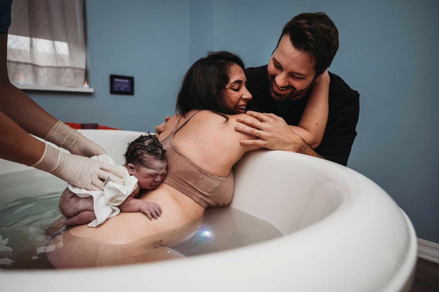 Water birth photo of couple welcoming newborn baby in birthing tub.