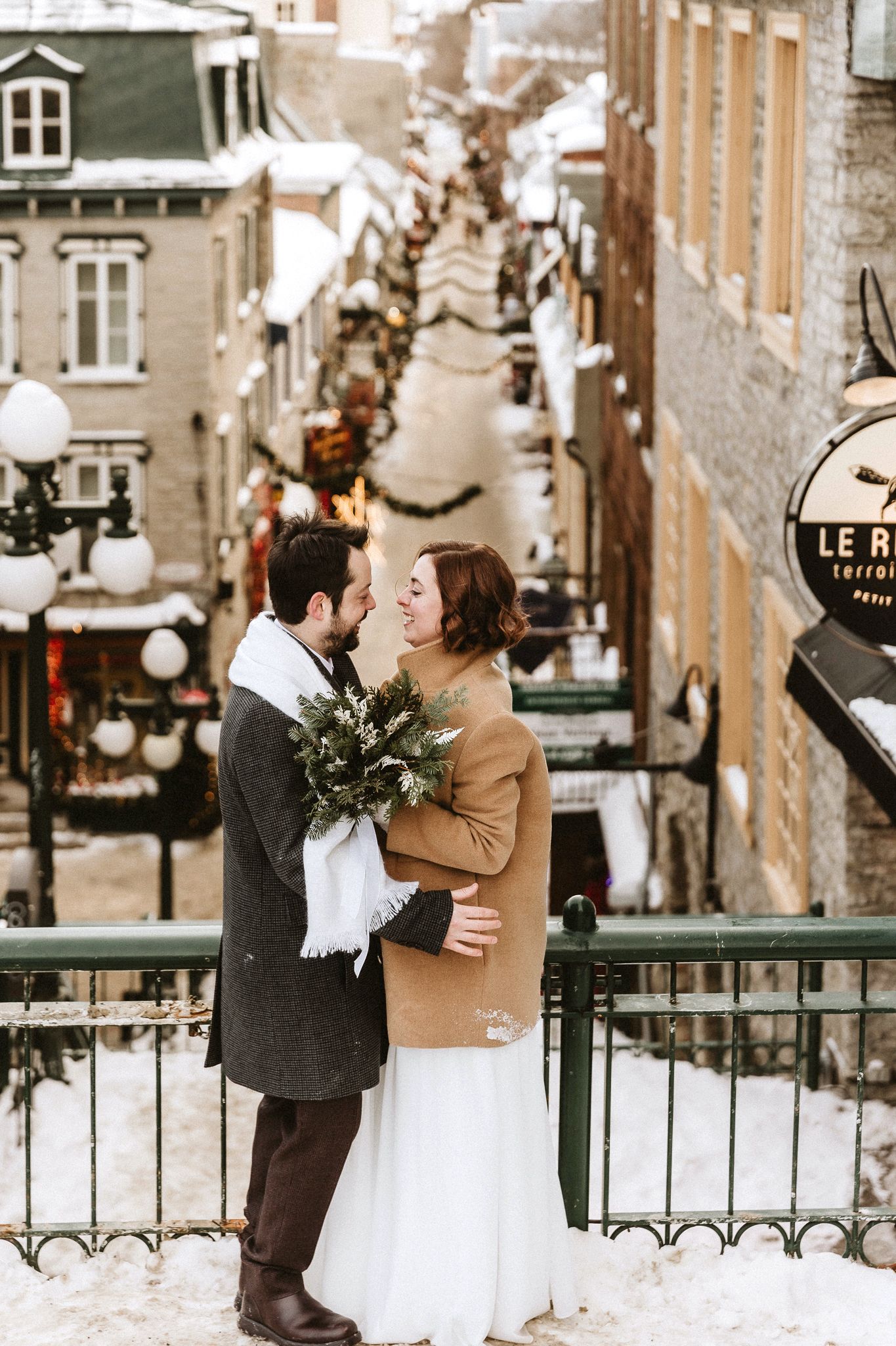 A romantic winter wedding portrait on a snowy European street with historic buildings.