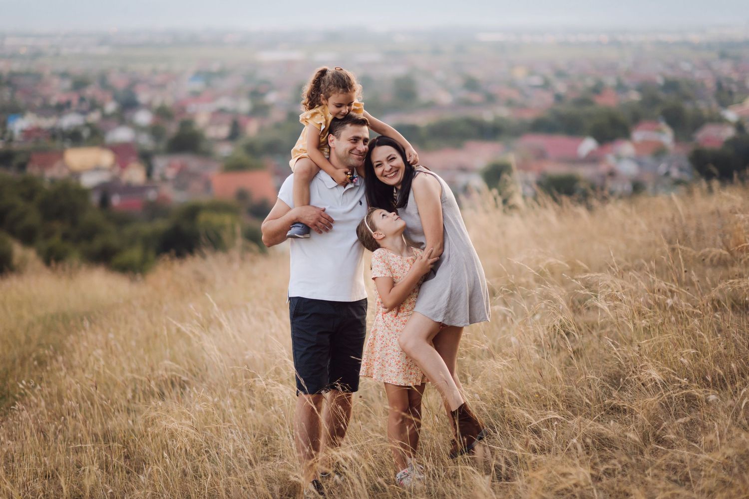 A family shares a playful moment together on a hilltop overlooking a town.
