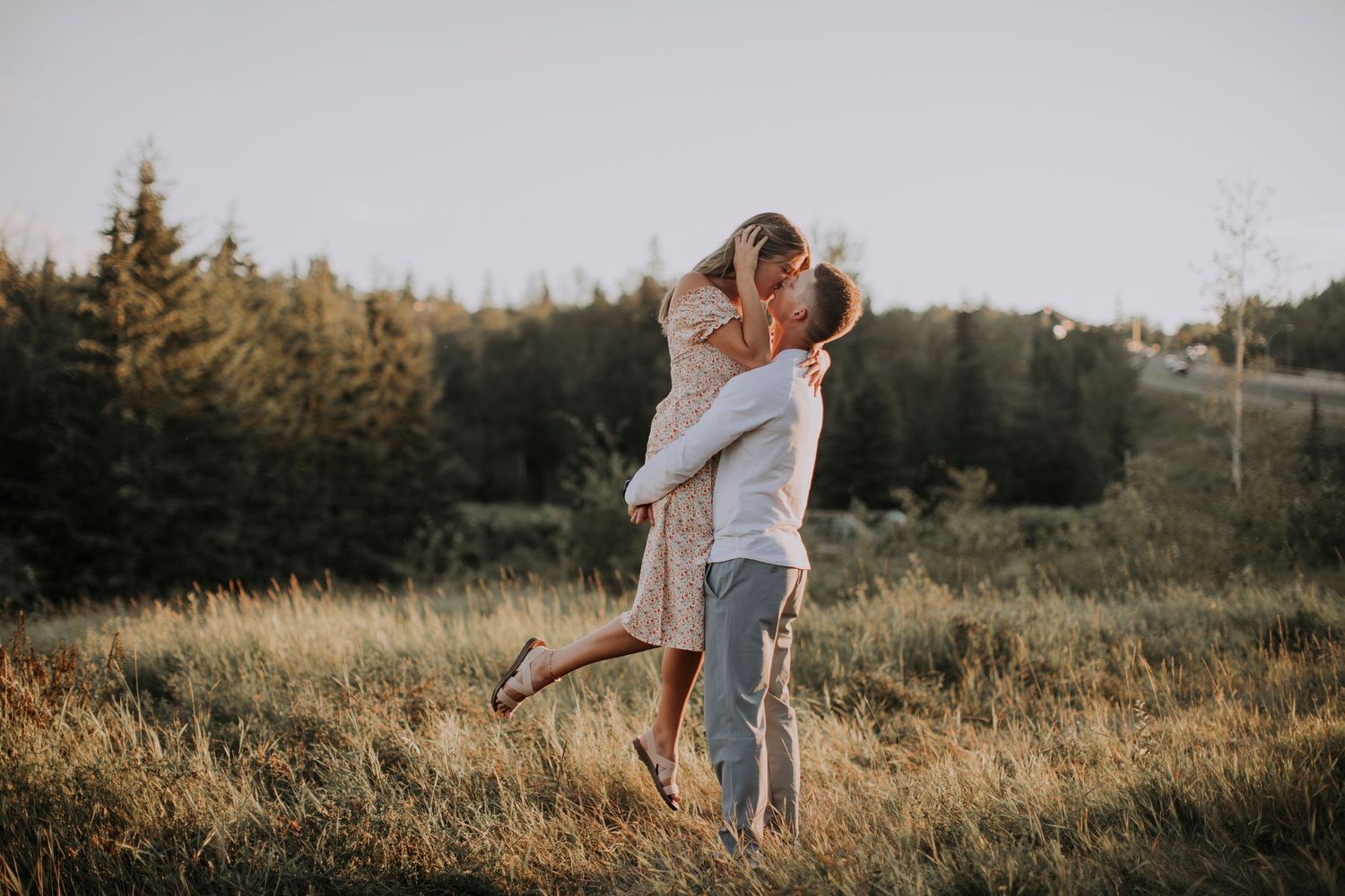Couple sharing a romantic moment in a sunlit meadow with forest backdrop.