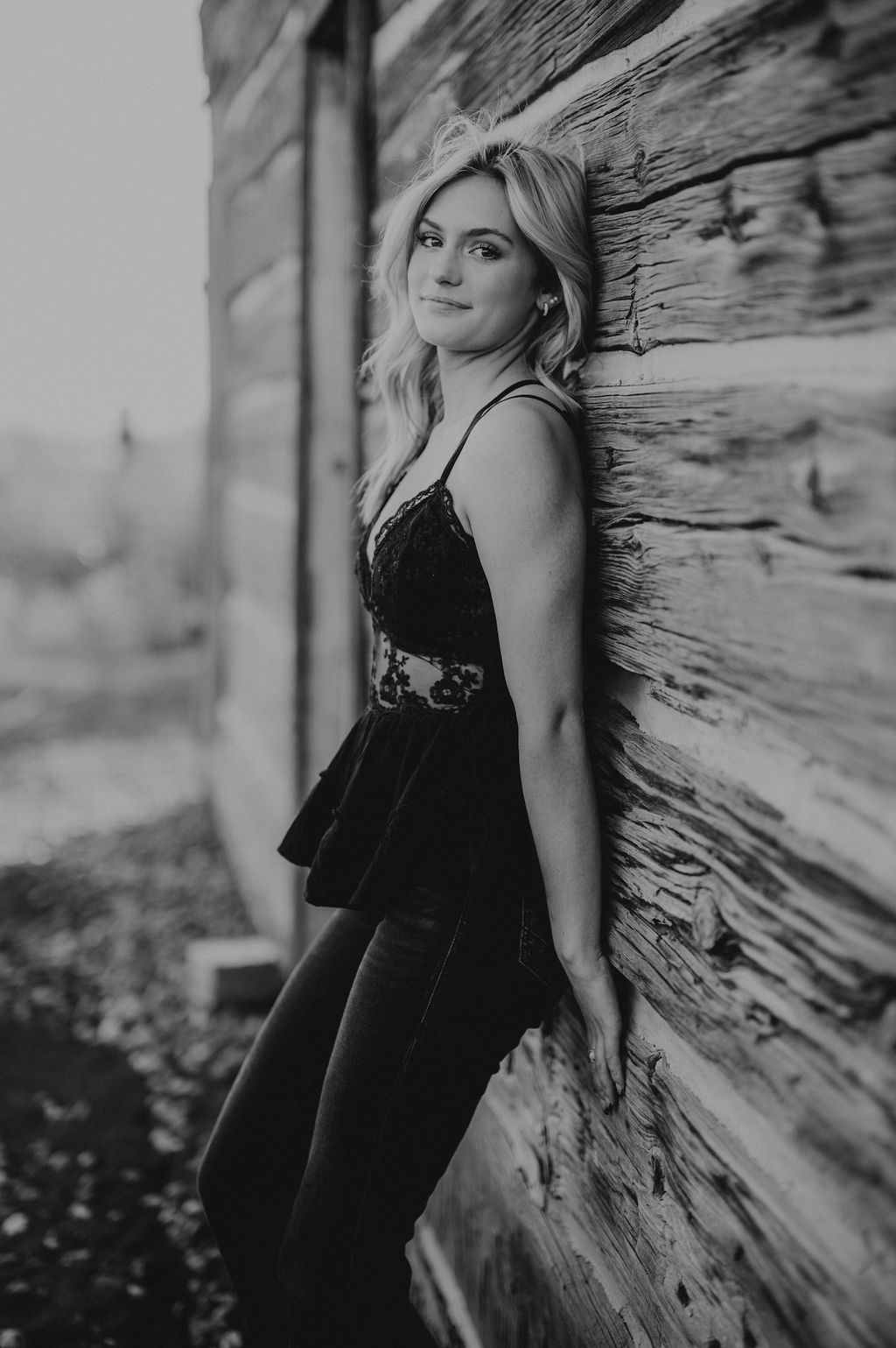 girl leaning up against and old cabin