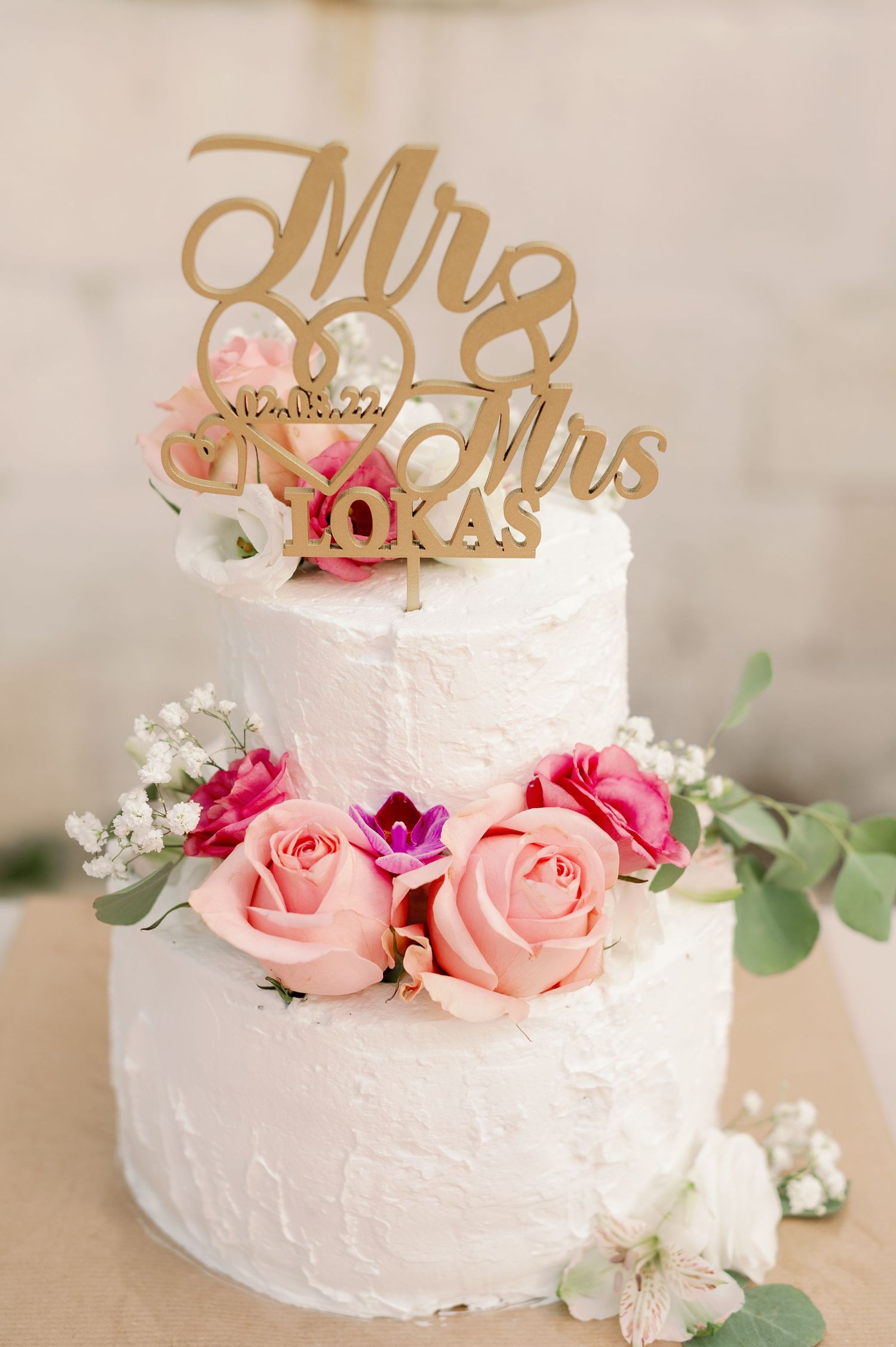 Two-tier white wedding cake decorated with pink roses and gold Mr & Mrs topper.