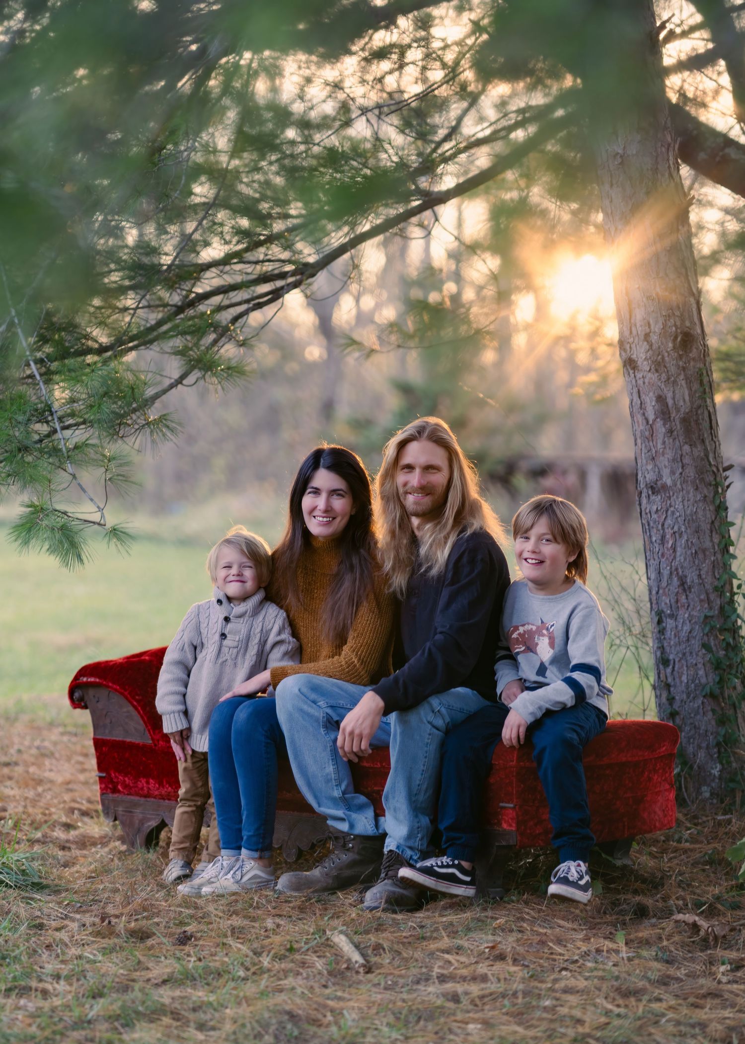Family of four sitting together on a red couch outdoors during sunset.