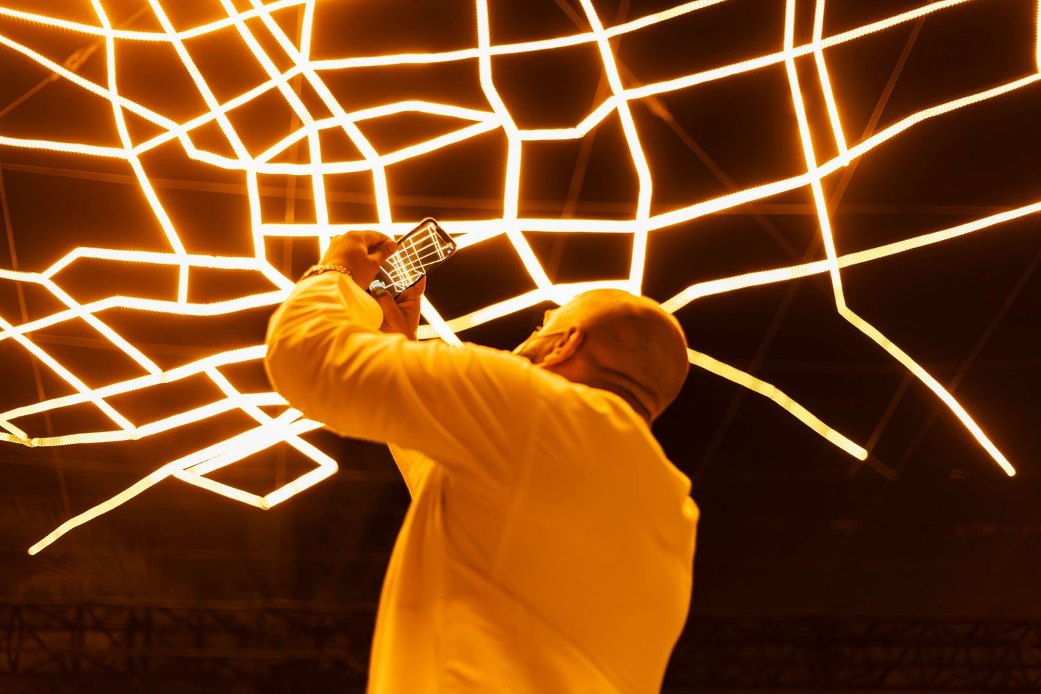 Person in yellow photographing geometric light installation on ceiling.