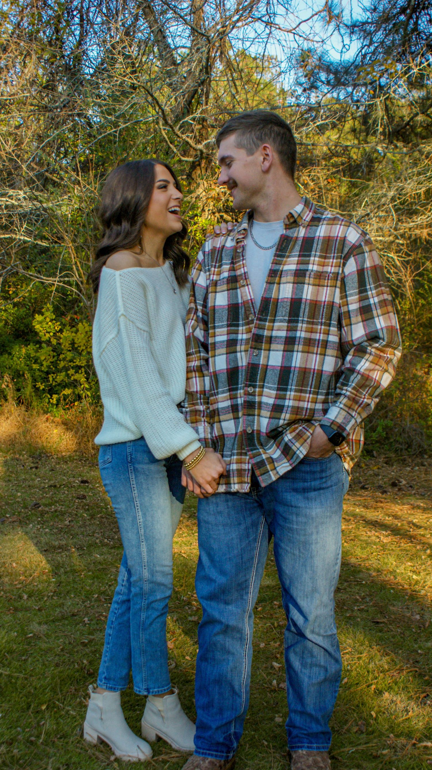 A couple sharing a joyful moment outdoors wearing coordinated casual outfits with plaid and sweaters.