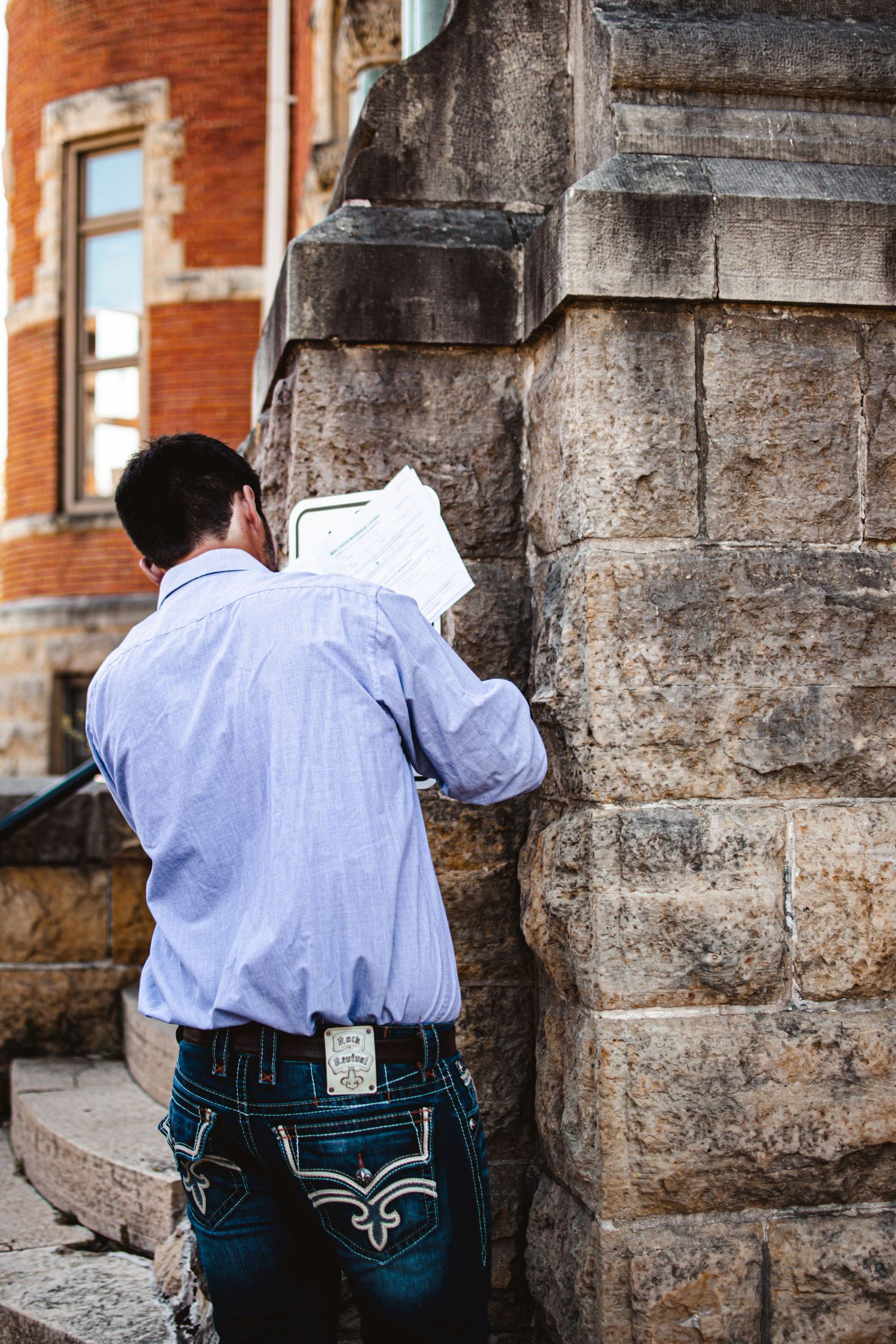Person in blue shirt writing on wall of historic brick building.