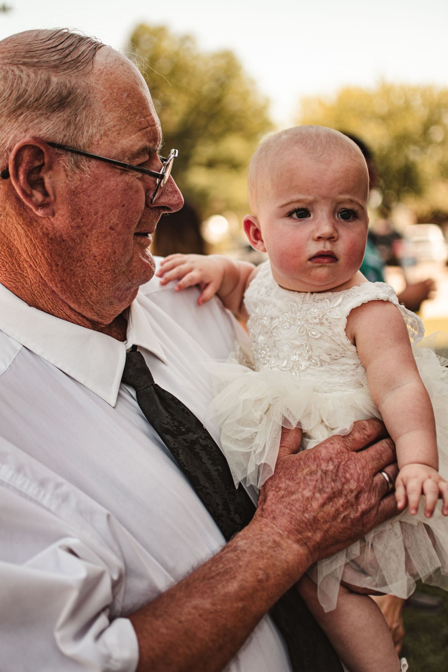 A small child in white dress being held outdoors.