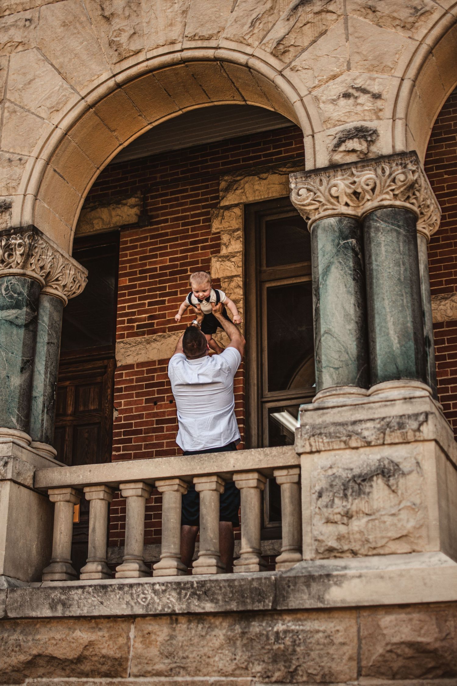 Photographer taking pictures from ornate stone balcony with classical columns.