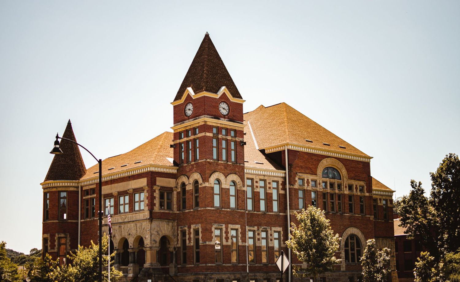 Historic red brick Victorian building with two towers and ornate architecture stands against a cloudy sky.