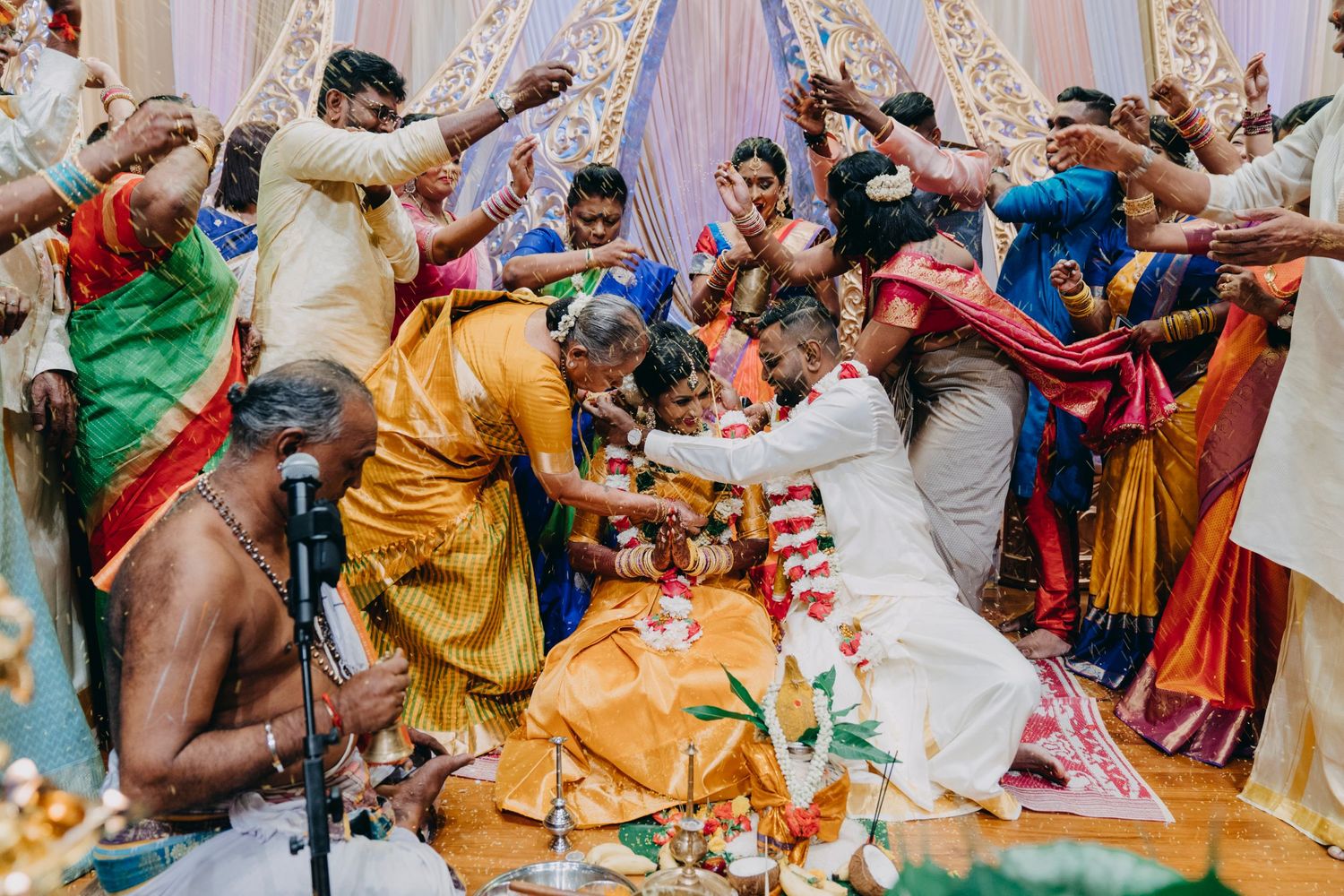 Row of colorfully dressed guests participate in joyful wedding celebration rituals.